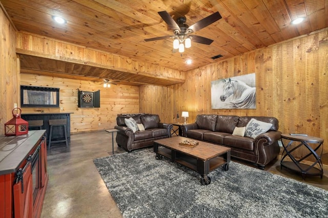 living area with wooden walls, wood ceiling, concrete flooring, and a ceiling fan