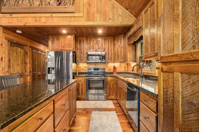 kitchen featuring a sink, appliances with stainless steel finishes, brown cabinetry, light wood finished floors, and wood ceiling