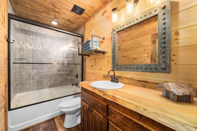 bathroom featuring toilet, wooden walls, shower / bath combination with glass door, wood ceiling, and vanity