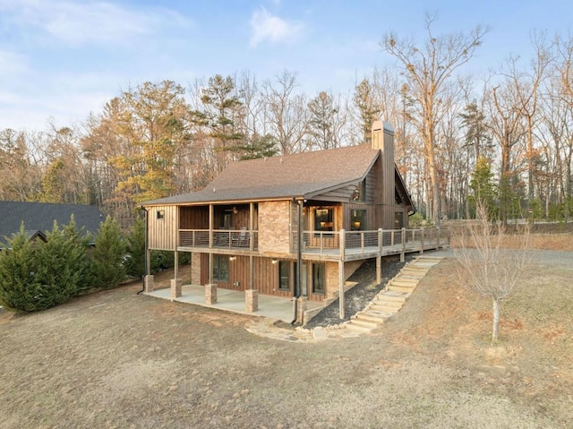 back of property with a patio, roof with shingles, a chimney, a deck, and board and batten siding