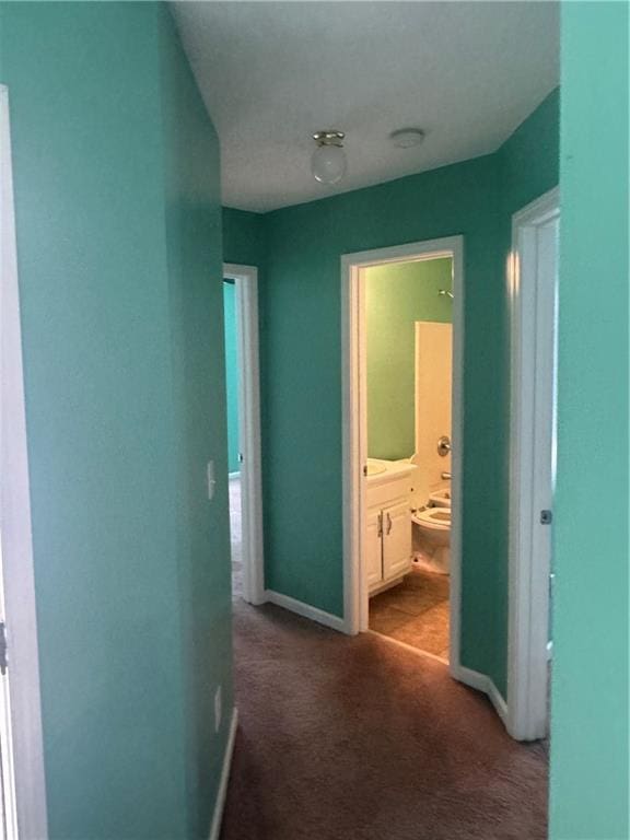 hallway featuring dark colored carpet and baseboards