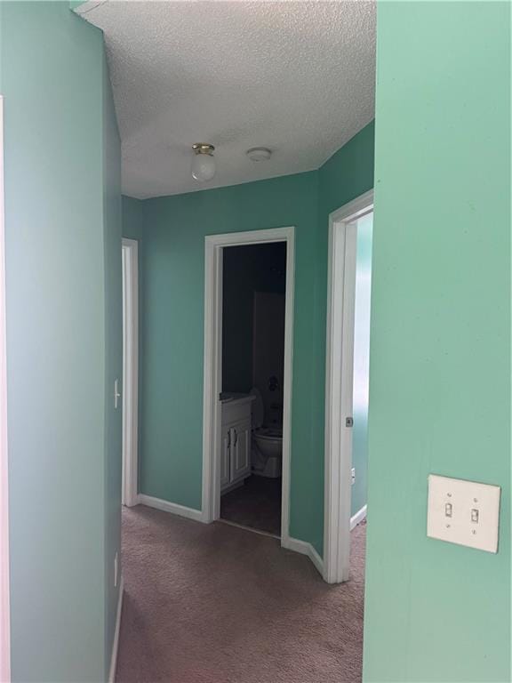 corridor with carpet floors, a textured ceiling, and baseboards