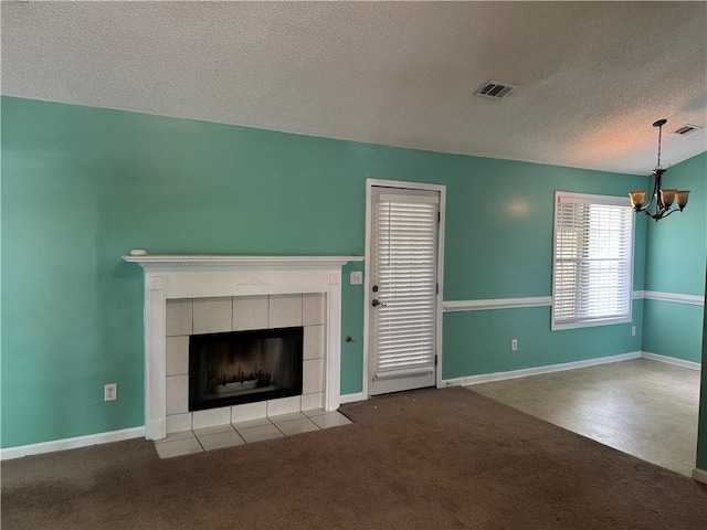 unfurnished living room featuring a tiled fireplace, a chandelier, visible vents, and a textured ceiling