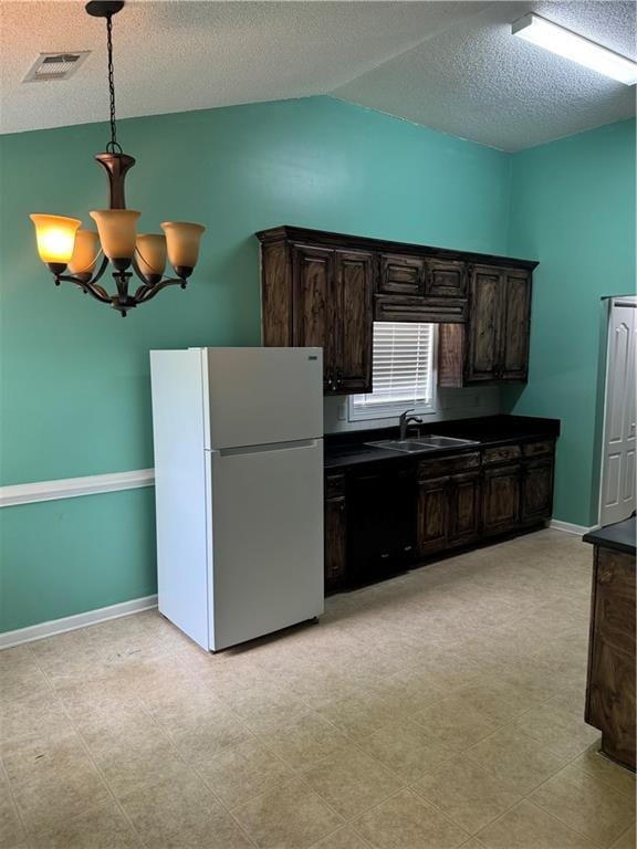 kitchen featuring vaulted ceiling, dark countertops, dark brown cabinets, a sink, and freestanding refrigerator