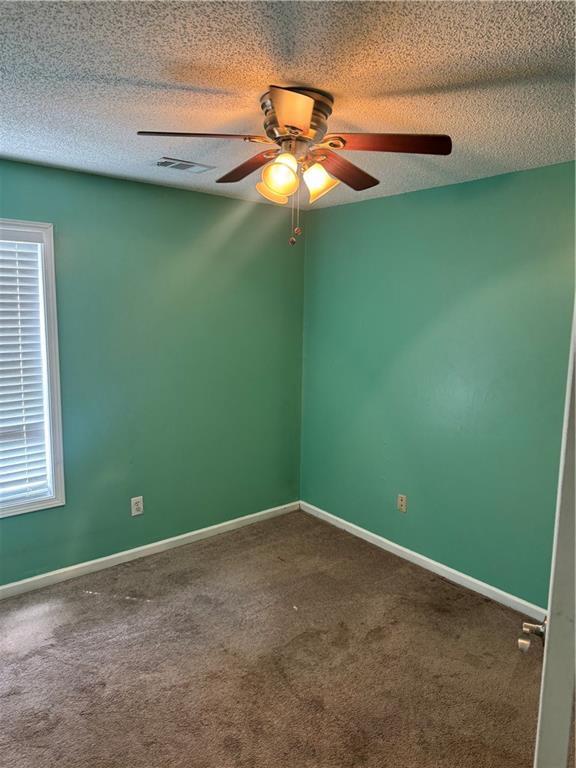 unfurnished room featuring carpet, visible vents, a ceiling fan, baseboards, and a textured ceiling