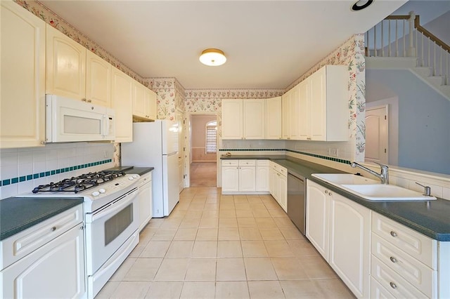 kitchen featuring white appliances, light tile patterned floors, wallpapered walls, dark countertops, and a sink