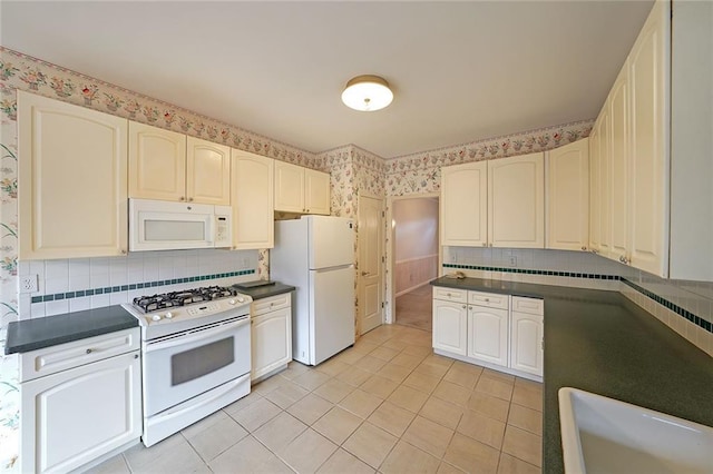 kitchen featuring dark countertops, white appliances, light tile patterned floors, and wallpapered walls