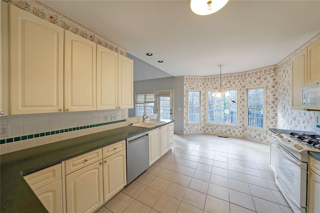 kitchen with wallpapered walls, white appliances, dark countertops, cream cabinets, and a sink