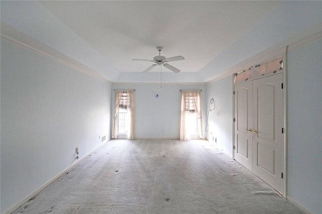 carpeted spare room with ceiling fan, a tray ceiling, and baseboards