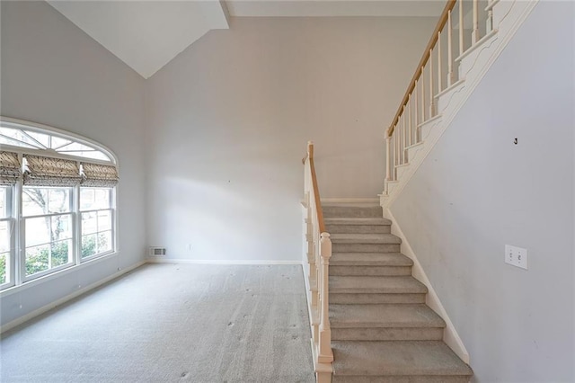 staircase with high vaulted ceiling, carpet floors, visible vents, and baseboards