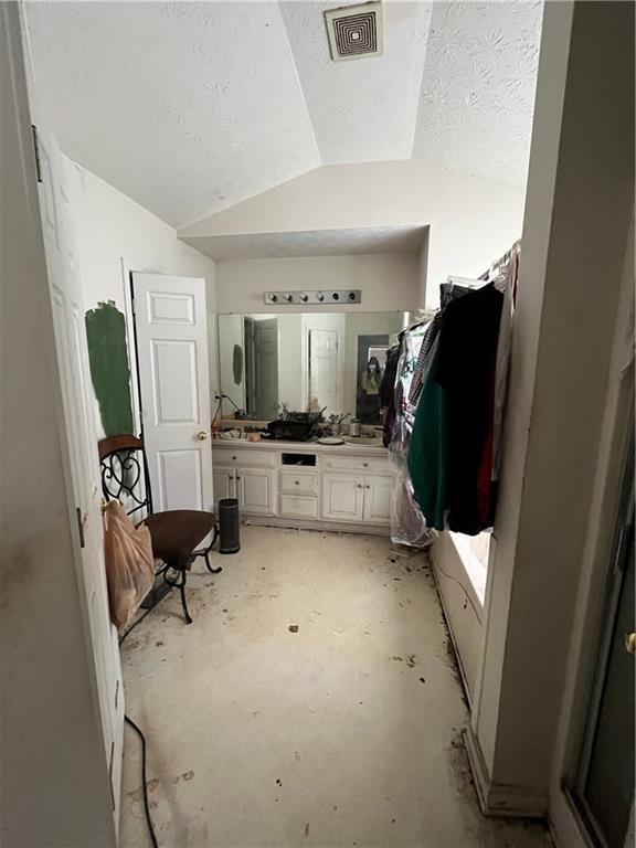 1528 Buckingham Pl, Stockbridge, GA 30281 - bathroom featuring vaulted ceiling, double vanity, concrete floors, and a textured ceiling
