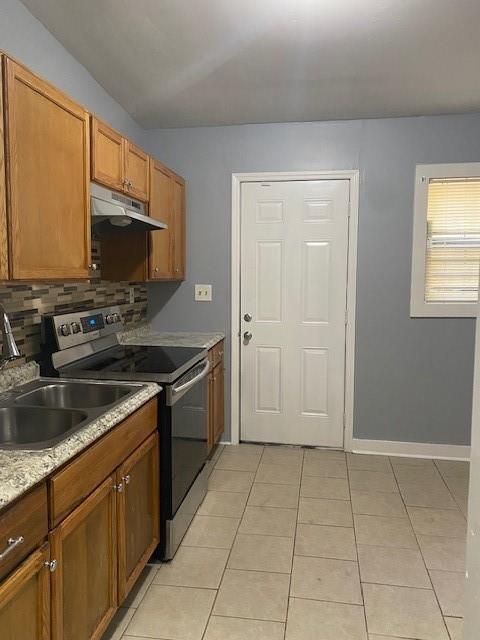 kitchen featuring light tile patterned flooring, sink, stainless steel range with electric cooktop, decorative backsplash, and light stone countertops