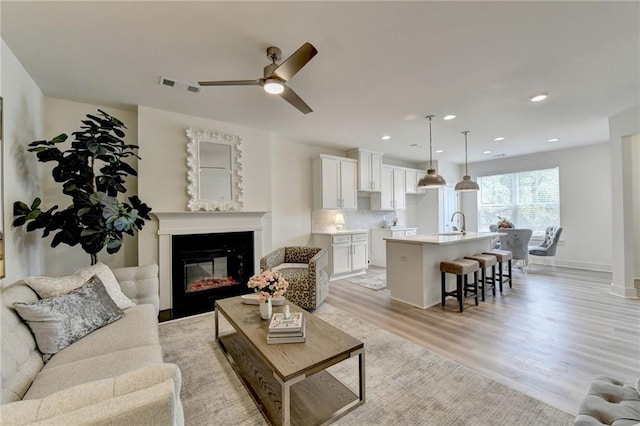 living room featuring ceiling fan, sink, and light hardwood / wood-style floors