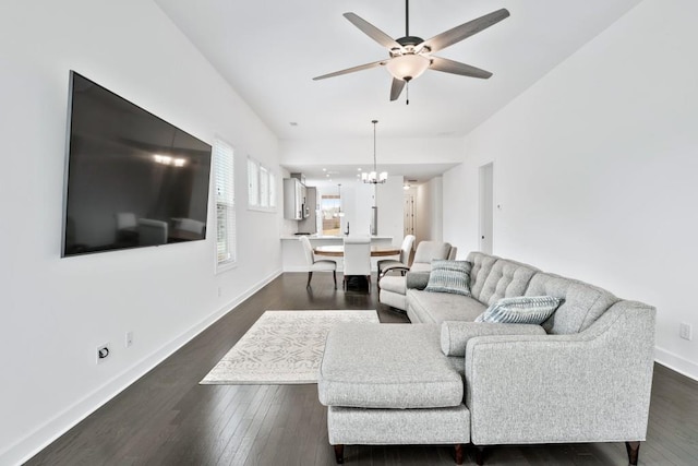 living room with ceiling fan with notable chandelier, dark wood-style flooring, and baseboards