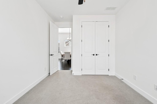 unfurnished bedroom featuring ceiling fan with notable chandelier, visible vents, baseboards, a closet, and carpet