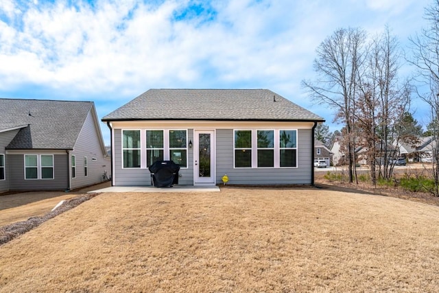 rear view of house featuring a shingled roof, a yard, and a patio