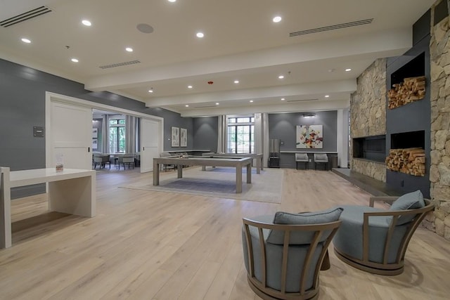 rec room with light wood finished floors, visible vents, beamed ceiling, and a stone fireplace