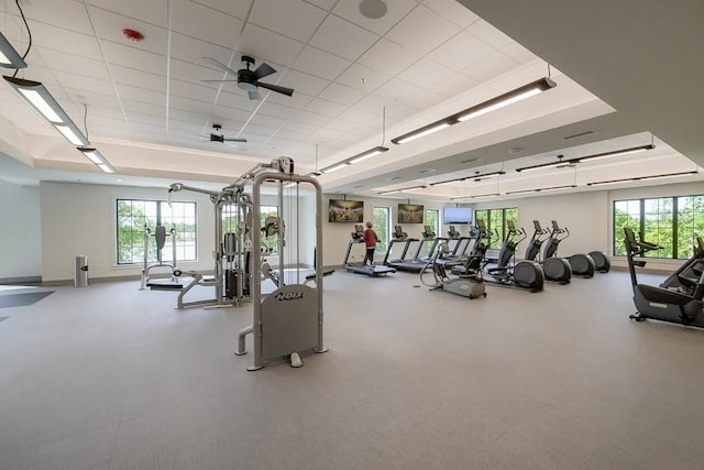 workout area featuring ceiling fan, baseboards, a raised ceiling, and a wealth of natural light