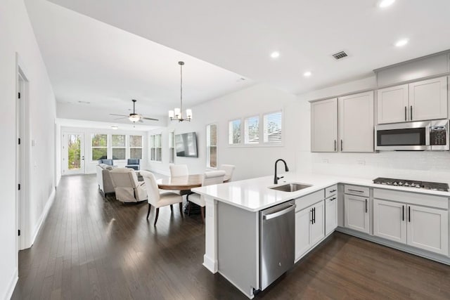 kitchen featuring tasteful backsplash, dark wood-style flooring, a peninsula, stainless steel appliances, and a sink