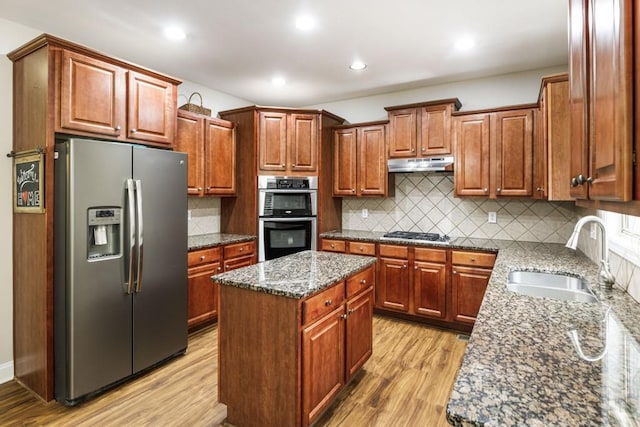 kitchen with a kitchen island, dark stone countertops, stainless steel appliances, under cabinet range hood, and a sink