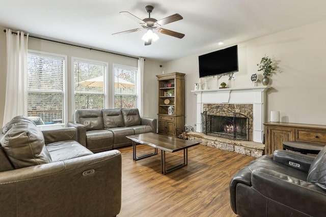 living area featuring ceiling fan, a stone fireplace, wood finished floors, and a healthy amount of sunlight