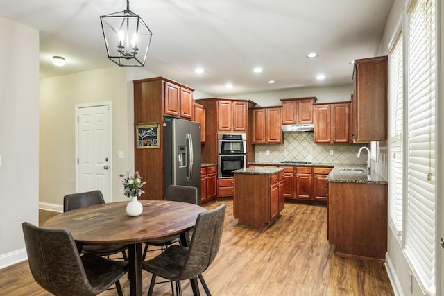 kitchen with under cabinet range hood, a sink, appliances with stainless steel finishes, a center island, and dark stone counters