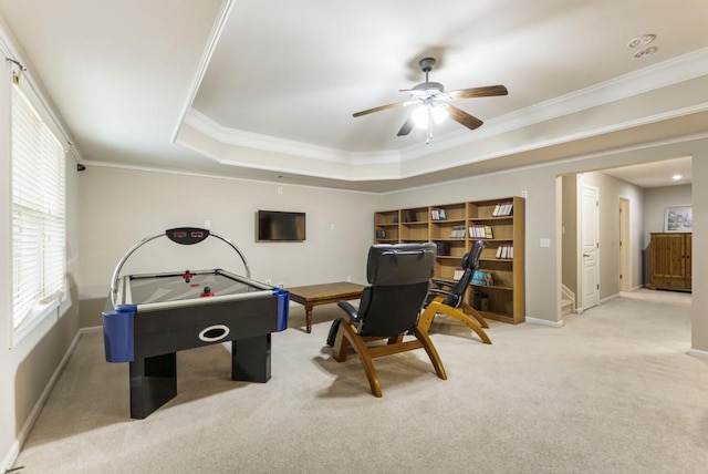 game room with baseboards, a raised ceiling, a ceiling fan, light colored carpet, and ornamental molding