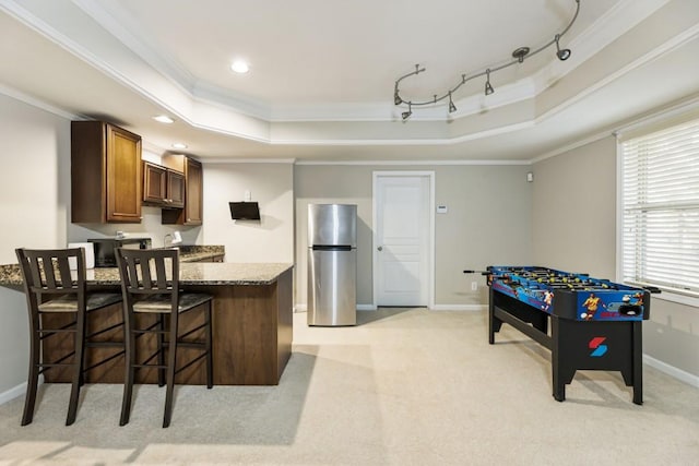 kitchen with a breakfast bar, ornamental molding, freestanding refrigerator, a tray ceiling, and dark stone countertops