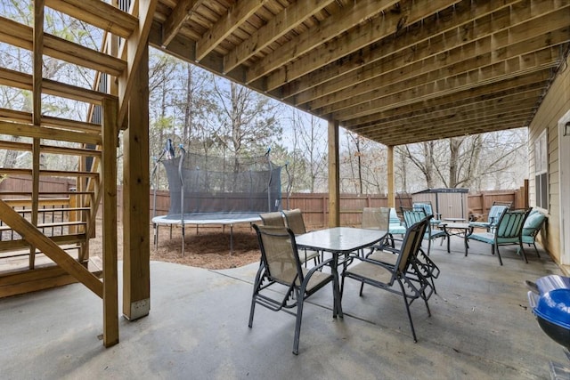 view of patio / terrace with a trampoline, an outbuilding, outdoor dining area, a storage unit, and stairway