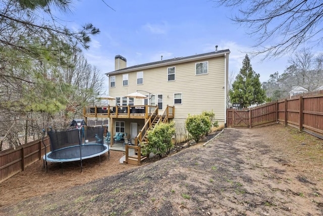 rear view of house with a trampoline, a chimney, stairway, a fenced backyard, and a wooden deck