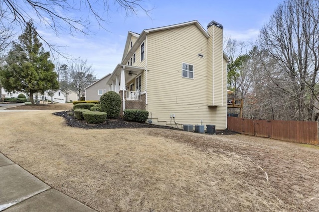 view of side of home featuring covered porch, a chimney, and fence