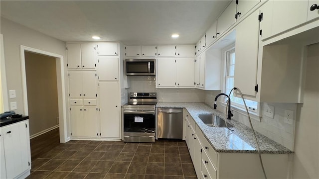 kitchen with stainless steel appliances, white cabinetry, sink, and light stone counters