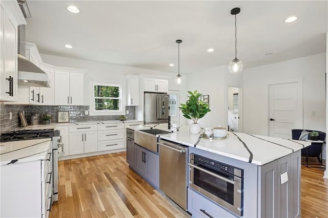 kitchen with decorative light fixtures, stainless steel appliances, white cabinets, and a center island with sink