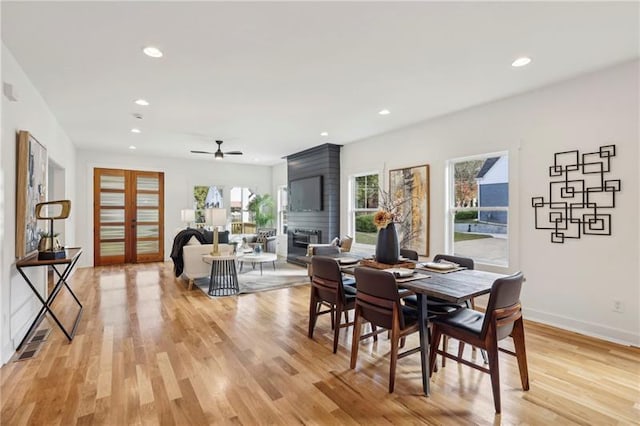 dining area with ceiling fan, a large fireplace, and light wood-type flooring