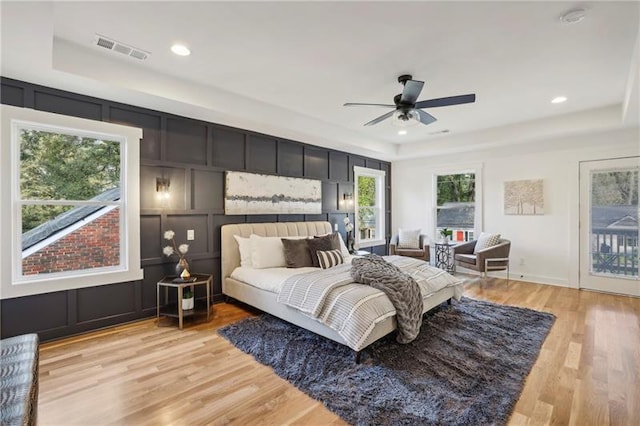 bedroom featuring ceiling fan, access to exterior, a raised ceiling, and light wood-type flooring