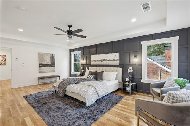 bedroom with ceiling fan, light wood-type flooring, and a tray ceiling