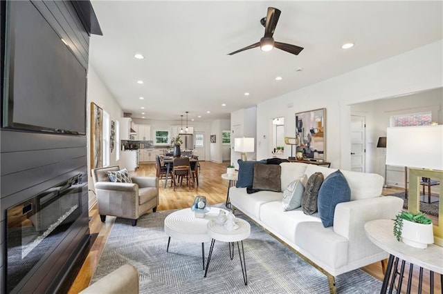 living room with ceiling fan, a large fireplace, and light wood-type flooring