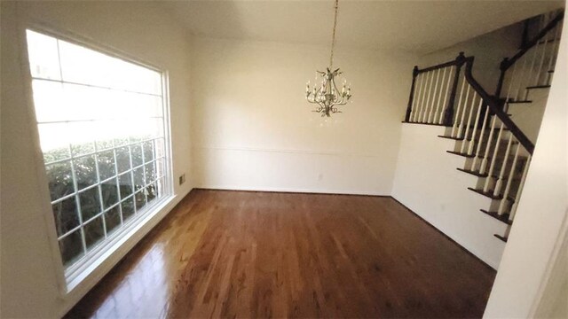 unfurnished dining area featuring dark wood-style floors, stairway, and a notable chandelier