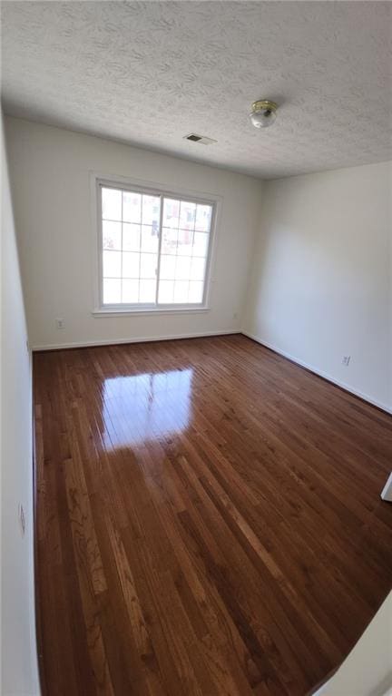 empty room featuring baseboards, a textured ceiling, visible vents, and dark wood-type flooring