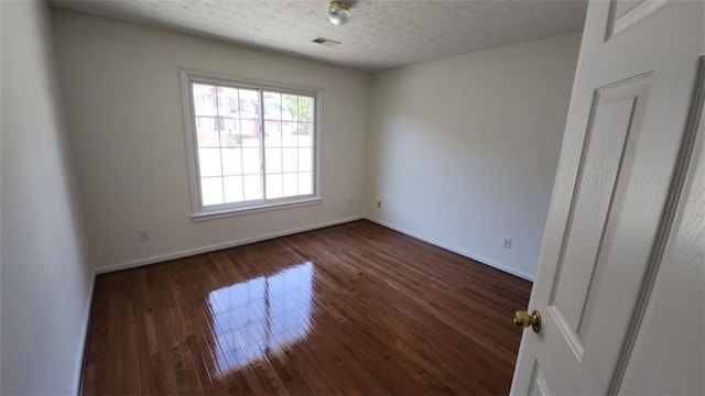 unfurnished room with a textured ceiling, dark wood finished floors, visible vents, and baseboards