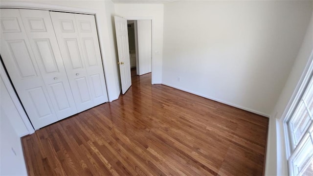 unfurnished bedroom with a closet, dark wood-style flooring, and baseboards