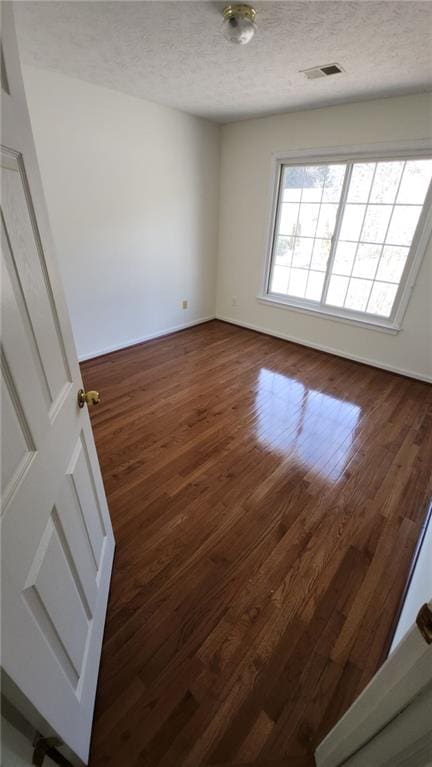 unfurnished room with baseboards, a textured ceiling, visible vents, and dark wood-type flooring