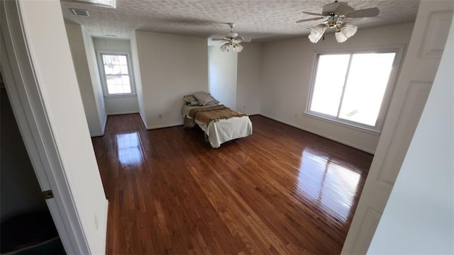 unfurnished bedroom featuring a textured ceiling, ceiling fan, visible vents, dark wood finished floors, and attic access