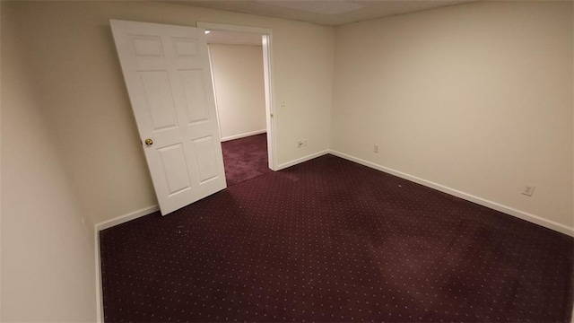 spare room featuring baseboards and dark carpet