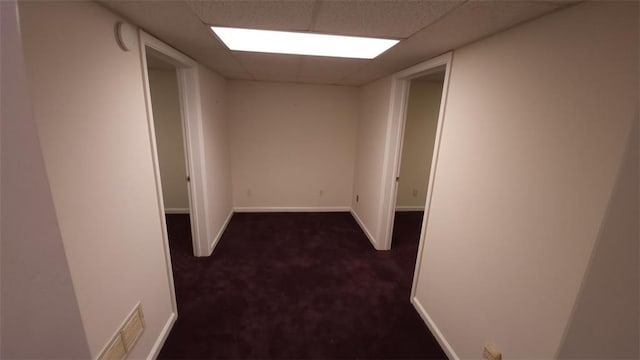 hall featuring a paneled ceiling, visible vents, dark carpet, and baseboards