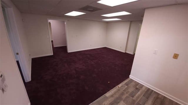 finished below grade area featuring dark wood-type flooring, a paneled ceiling, and baseboards