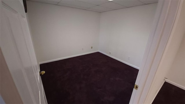 empty room with baseboards, dark colored carpet, and a drop ceiling