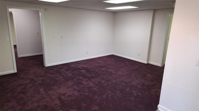 unfurnished room featuring a drop ceiling, dark carpet, and baseboards