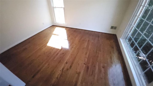 unfurnished room with dark wood-style floors, visible vents, and baseboards