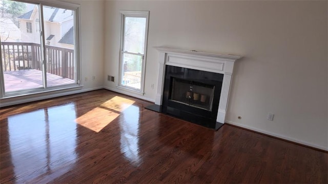 unfurnished living room featuring dark wood-type flooring, a glass covered fireplace, a healthy amount of sunlight, and baseboards